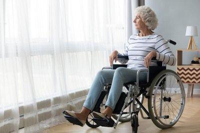 elderly woman sitting on a wheelchair looking outside of the window of her house.jpg